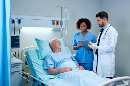 Senior man lying in hospital bed interacting with young Black woman nurse and young man doctor discussing medical care using digital tablet