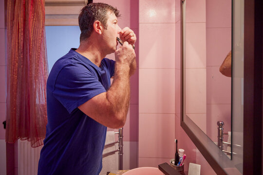 middle-aged man in the bathroom in the morning brushing his teeth, shaving and styling his hair - Powered by Adobe