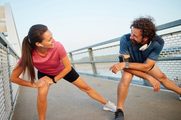 Two individuals are engaged in a stretching routine on a scenic bridge, enjoying the fresh air during a morning workout. Their smiles and relaxed posture reflect a commitment to fitness and health.
