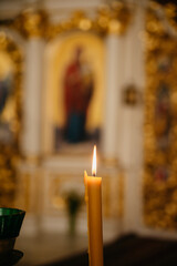 A lit candle stands in a church against the background of an icon
