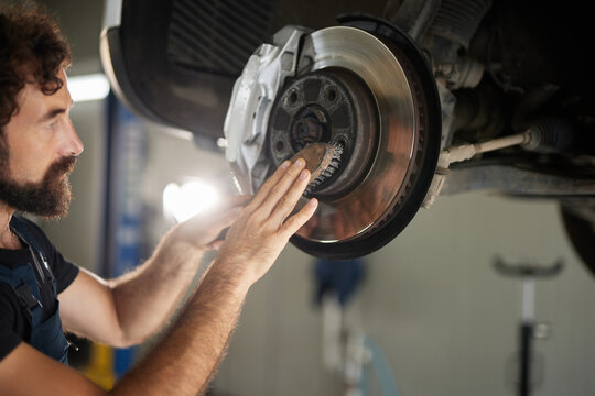 A skilled mechanic works on a car's brake system in an auto shop. He inspects and adjusts essential components to ensure safety and proper function. Tools are neatly arranged nearby.