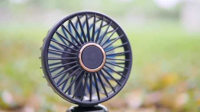 Mini fan black, battery-operated, portable on dry leaves on the ground.