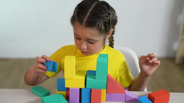 Girl building colorful block tower with concentration while child plays at table, toy block stacked to build shape, learning through playful activity and preschool play fostering fine motor skill