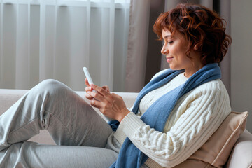 young woman sitting on sofa using smartphone for telemedicine consultation smiling and interacting with healthcare provider in modern home setting