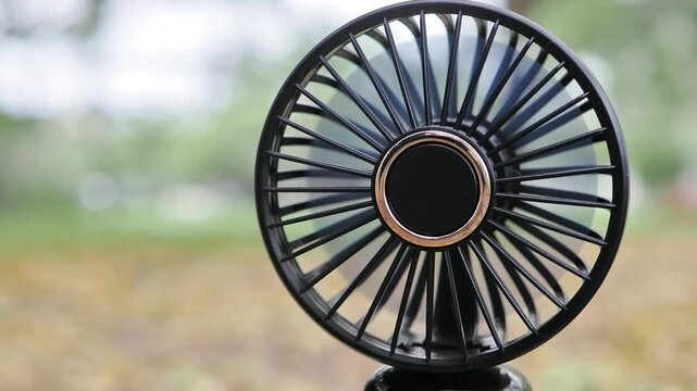 Mini fan black, battery-operated, portable on dry leaves on the ground.