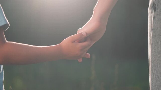 Child fingers meet parent palm. Supportive touch in sunlight. Connection through hands shows love. Together parent and child share moment of care. Hands holding in nature. Gentle child parent contac