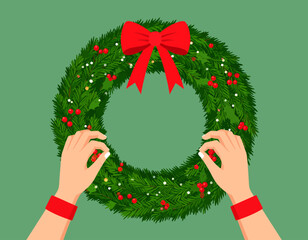 Hands holding a festive Christmas wreath decorated with a red bow, berries, and lights, set against a green background.