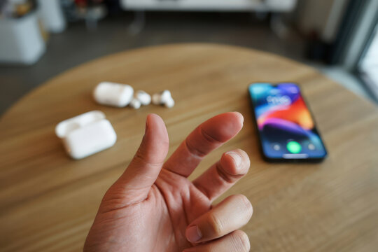 Focus on a person's outstretched hand over a wooden table, with out-of-focus wireless earbuds and smartphone nearby, representing personal connection to technology and the daily digital lifestyle. - Powered by Adobe