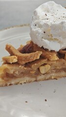 Slice of apple pie with nuts topped with a scoop of vanilla ice cream on a white plate. this image conveys sweetness, comfort and cozy dessert enjoyment