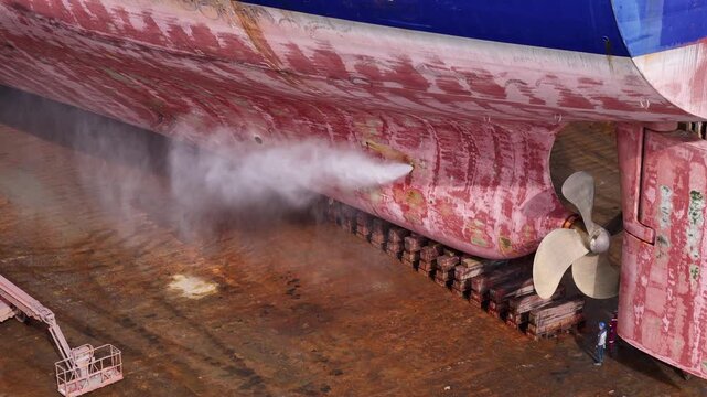 High-pressure water cleaning process on ship hull in dry dock for maintenance and rust removal. Essential marine engineering task for ship repair, safety, and performance.