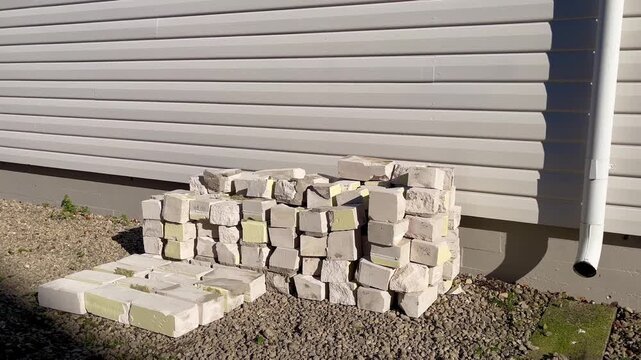 Stack of used silicate bricks with chipped edges and traces of old insulation leaning against light-colored wall