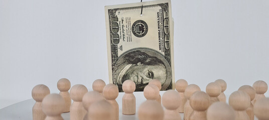 Wooden Figures Surrounding A Hanging One Hundred Dollar Bill