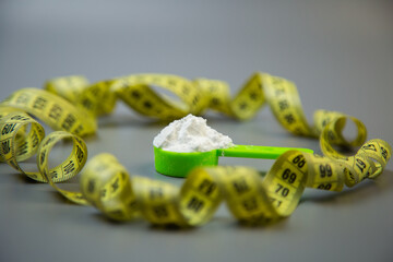 Green scoop with white powder is placed amidst a curled yellow measuring tape, representing health, fitness, and nutrition themes in a contemporary setting