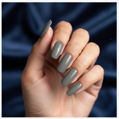 Close-up of a hand with long gray glossy acrylic nails against a smooth blue background, showcasing modern manicure style.
