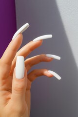 Close-up of a hand with long white glossy acrylic nails against a smooth blue background, showcasing elegant manicure style.