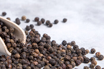 Close-up of Black Peppercorns Spilling from Wooden Scoop on Light Grey Background