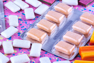 Orange and White Chewing Gum Tablets in a Blister Pack and Scattered on a Pink Background