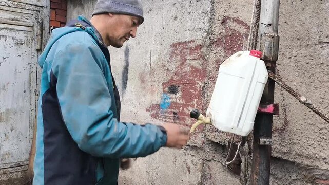 A man working in heavy industrial work washes his dirty hands with water from a makeshift washbasin