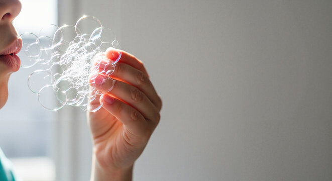 Child blowing soap bubbles while holding them in hand indoors