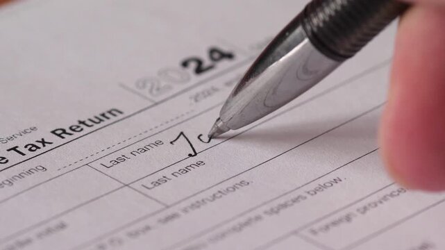 Macro view: man&rsquo;s hand filling out IRS 1040 tax form with a pen, symbolizing annual income reporting and tax paymen