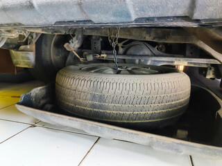 A spare tire is removed from the storage area under the rear of the car to replace a flat tire.