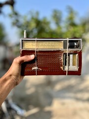 Hand Holding a Classic Analog Shortwave Radio Receiver Wrapped with Twine, Showing Wear and Age Against a Blurred Natural Background.