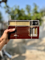 Hand Holding a Classic Analog Shortwave Radio Receiver Wrapped with Twine, Showing Wear and Age Against a Blurred Natural Background.