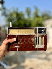 Hand Holding a Classic Analog Shortwave Radio Receiver Wrapped with Twine, Showing Wear and Age Against a Blurred Natural Background.