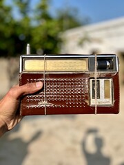 Hand Holding a Classic Analog Shortwave Radio Receiver Wrapped with Twine, Showing Wear and Age Against a Blurred Natural Background.