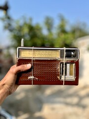 Hand Holding a Classic Analog Shortwave Radio Receiver Wrapped with Twine, Showing Wear and Age Against a Blurred Natural Background.