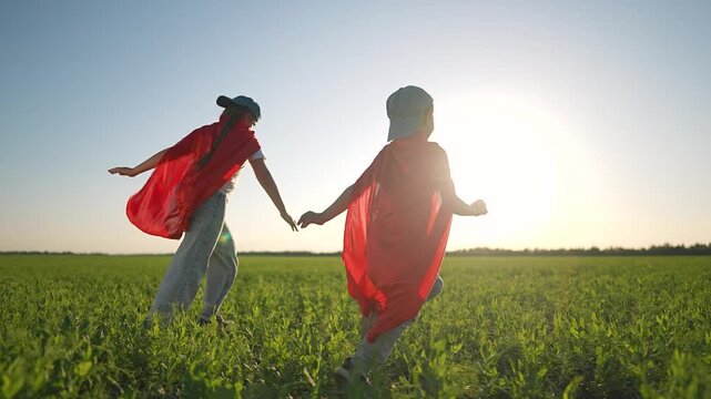 Boy and girl play superhero running together. Children cape chase dreams on summer field. Outdoor fun for children with superhero cape. Happy boy and happy girl running. Field echo with children joy.