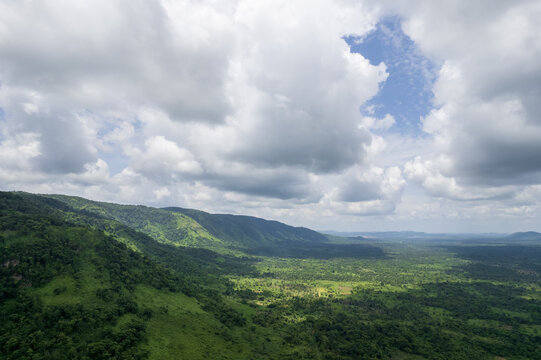Aerial view of mountains covered in dense green forests under a sky filled with fluffy white clouds, Erin Ijesa, Osun state, Nigeria.