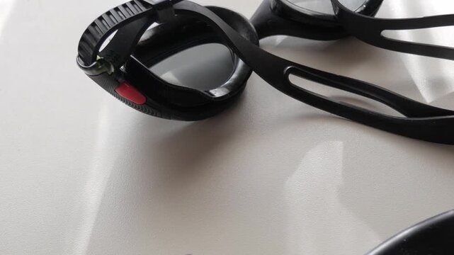 Macro shot of black swimming goggles with reflections on white surface under soft daylight.