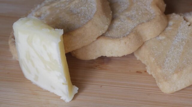 Shortbread biscuits served on a wooden board with a slice of butter placed beside them.