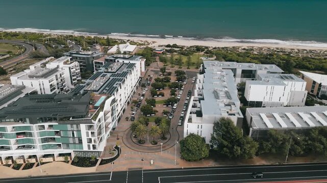 Cinematic aerial footage showing an advance from the train station towards North Fremantle and then to the beach, where the Indian Ocean waves crash onto the beautiful white sandy beach,