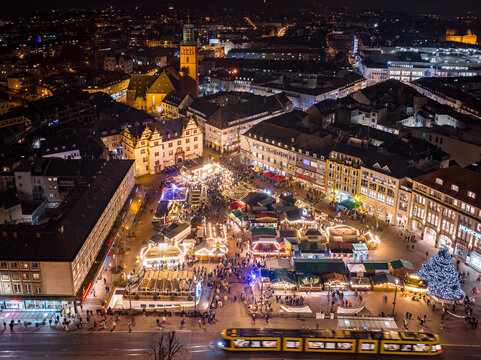 Aerial view of the illuminated Christmas market glows warmly against the dark cityscape, featuring the distinctive Stadtturm tower in the background, Darmstadt, Hessen, Germany.
