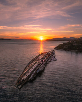 Aerial view of the abandoned MS Mediterranean Sky shipwreck resting in vibrant turquoise waters during a warm sunset near Athens, Greece.