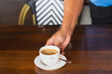 Waiter serving cup off coffee on wooden table in cafe.