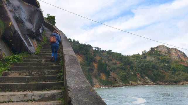 woman in climbing stone steps along the coastal cliff path spain faro de la plata