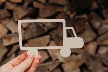 Hand holding a truck silhouette against a stack of firewood — wood delivery, forestry and logistics concept