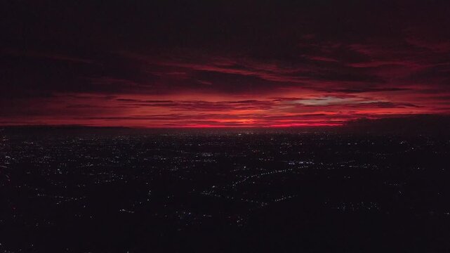Aerial view of city lights twinkling under a vibrant red and orange sunset sky, creating a stark contrast between light and dark, Klaten Regency, Central Java, indonesia.