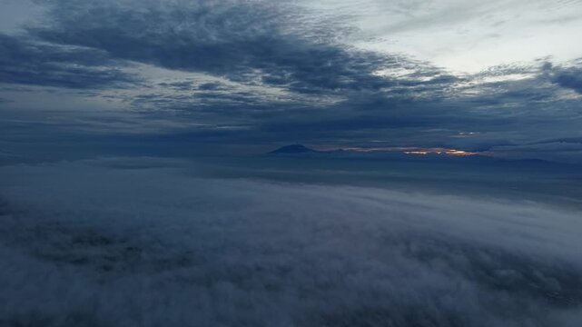 Aerial view of the landscape shrouded in dense fog, with a mountain range silhouetted against the horizon, Klaten Regency, Central Java, Indonesia.