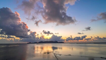 A serene seascape at dusk reflects a vibrant, cloud-filled sky, with an island silhouette on the horizon