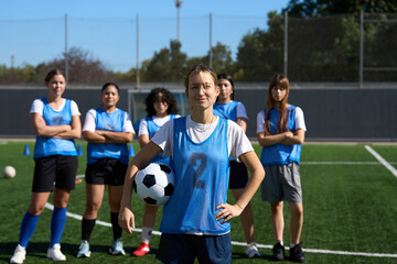 Female soccer player holding ball with team on pitch