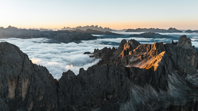 Aerial view of rugged peaks pierce through a sea of ethereal clouds, kissed by the first light of dawn, Karersee, Trentino-South Tyrol, Italy.
