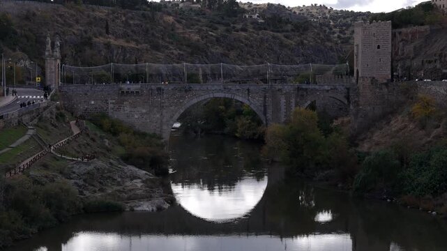 Aerial view of the historic Puente de San Martin bridge with its stone arches reflected in the calm river below, Toledo, Castile-La Mancha, Spain.