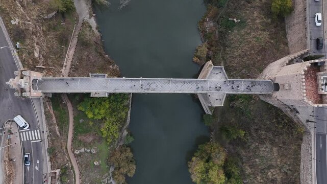 Aerial view of the historic San Martin bridge spanning the river, its stone contrasting with the lush greenery along the banks, Toledo, Castile-La Mancha, Spain.