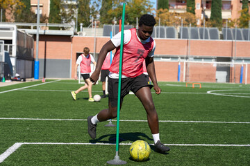 Young athlete training for soccer dribbling around agility pole