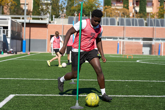 Young athlete training for soccer dribbling around agility pole