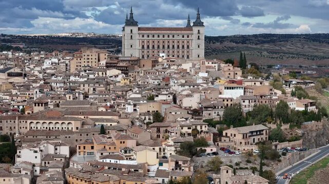 Aerial view of the Alcazar fortress standing tall over the ancient city with its terracotta rooftops under a cloudy sky, Toledo, Castile-La Mancha, Spain.